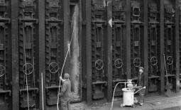 Photo d'ouvriers pulvérisant un revêtement réfractaire au sein d'un haut fourneau, dans les années 1960